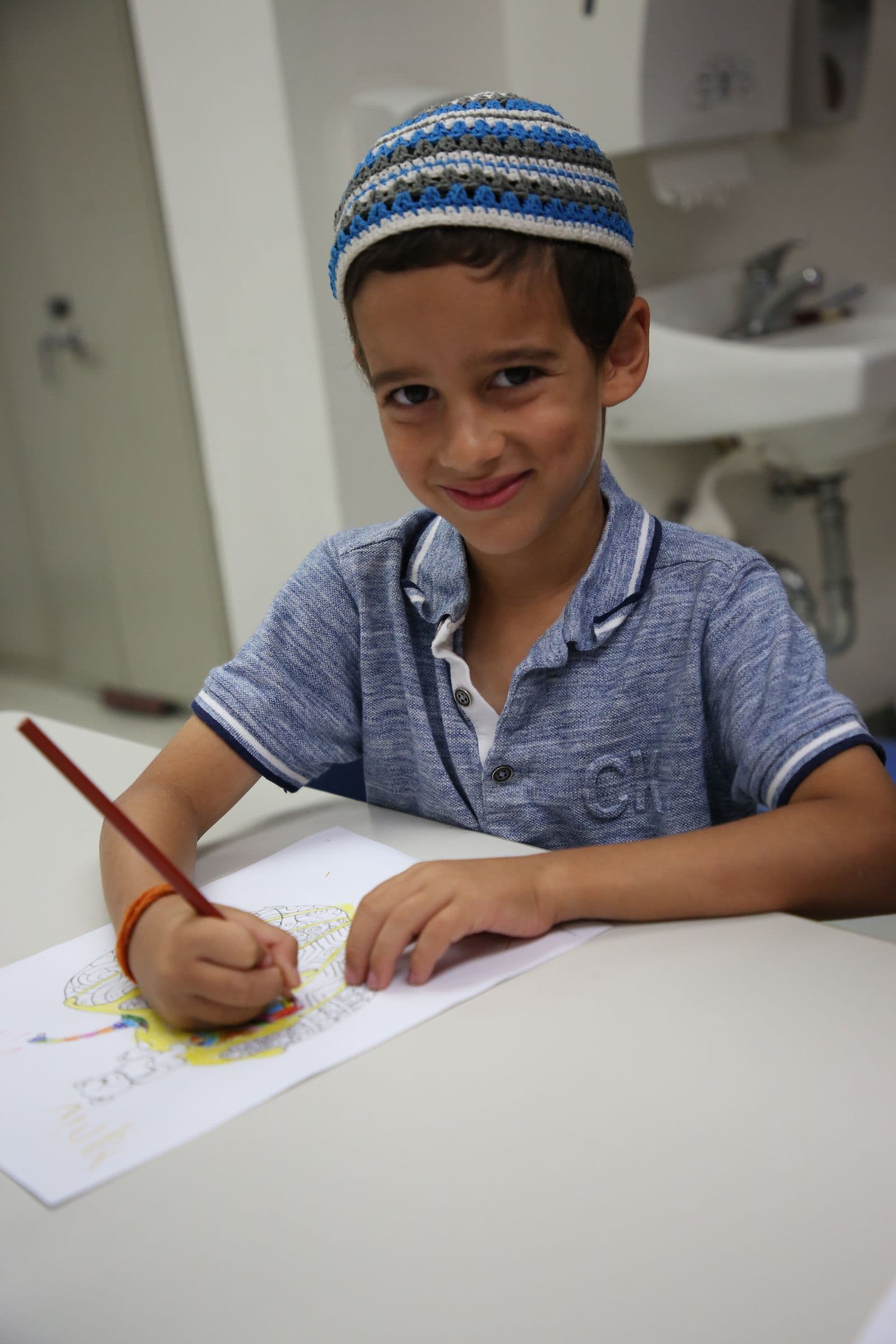 A young student drawing in a classroom at Kadima Jewish day school
